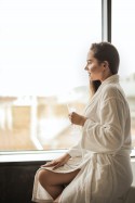 woman drinking alone in white robe gazing out the window